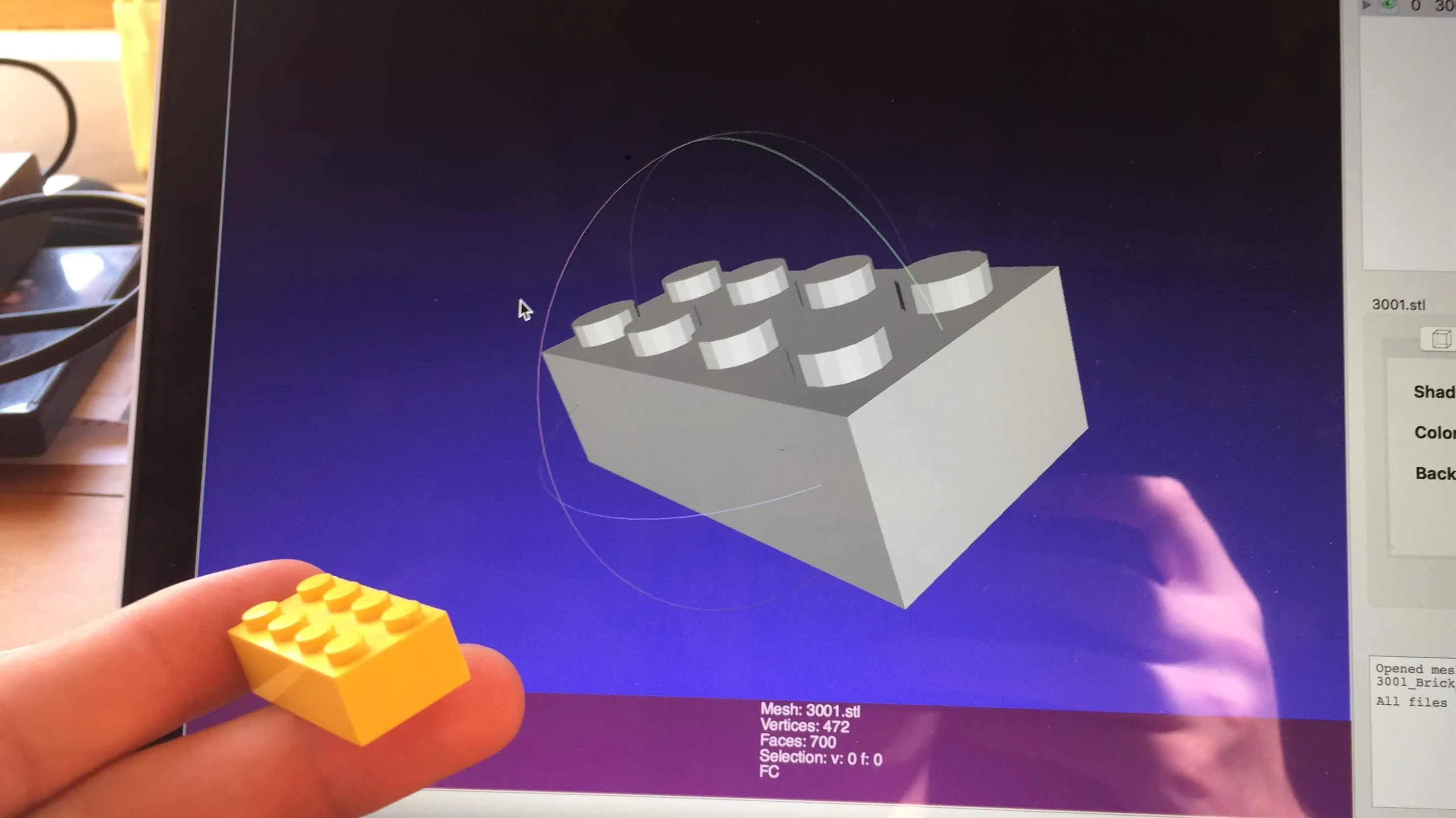 A yellow LEGO brick held next to a 3D brick model on a screen